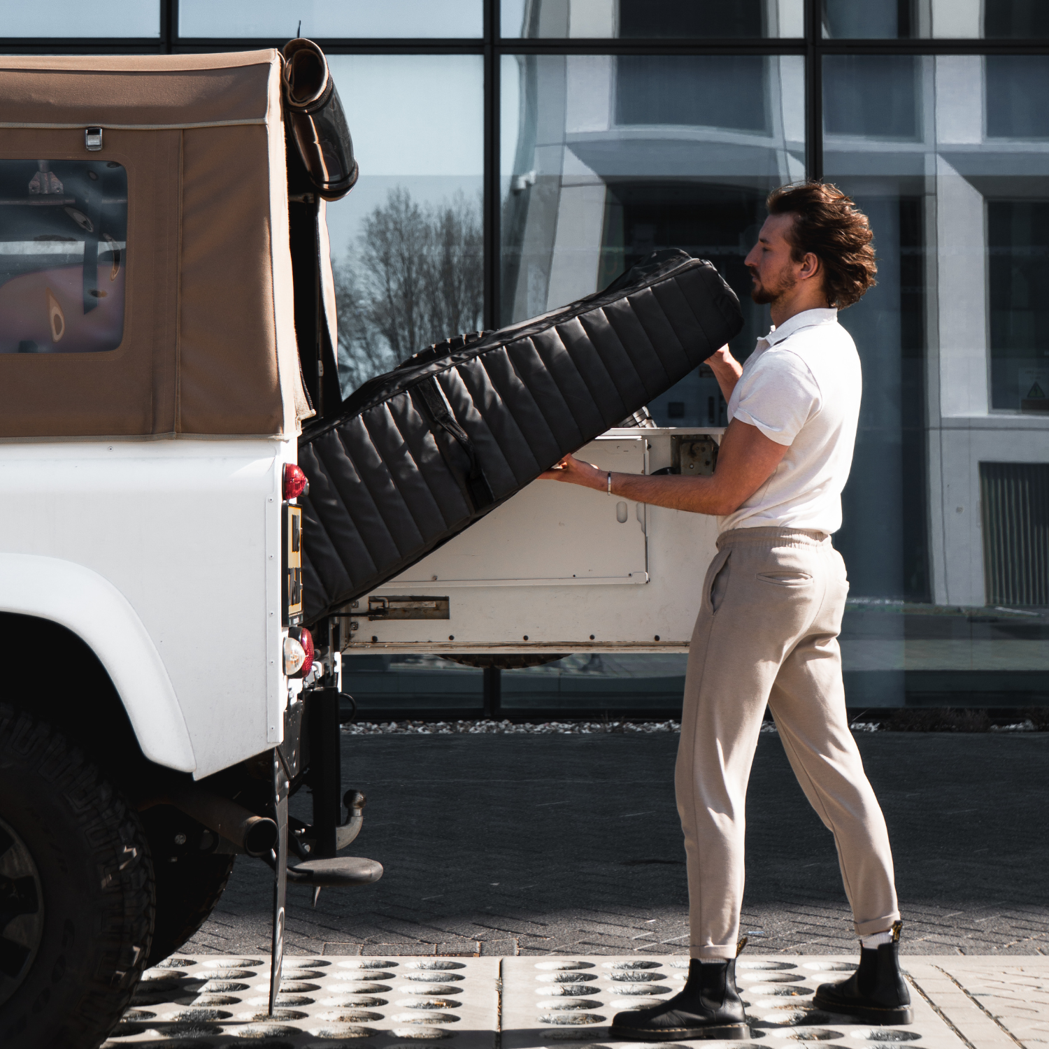 Man loading a Sportr Golf Travel Bag into the back of a Landrover near a building.
