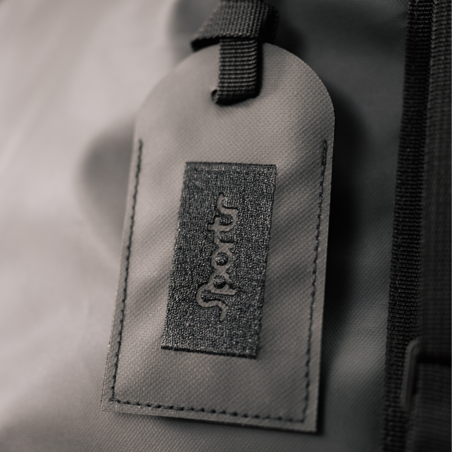 Gray/blackfabric tag with a Sportr logo on a textured gray background