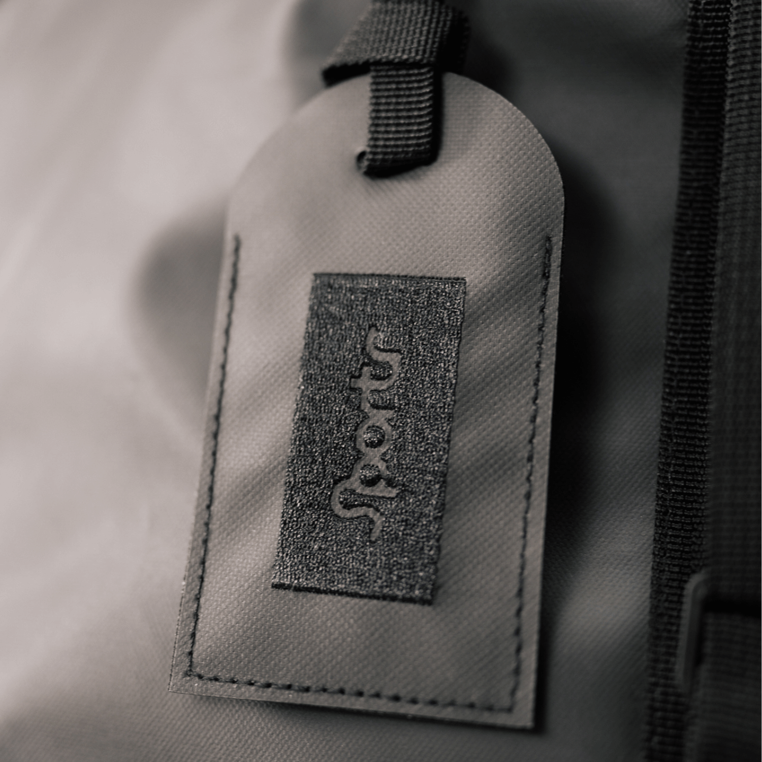 Gray/blackfabric tag with a Sportr logo on a textured gray background