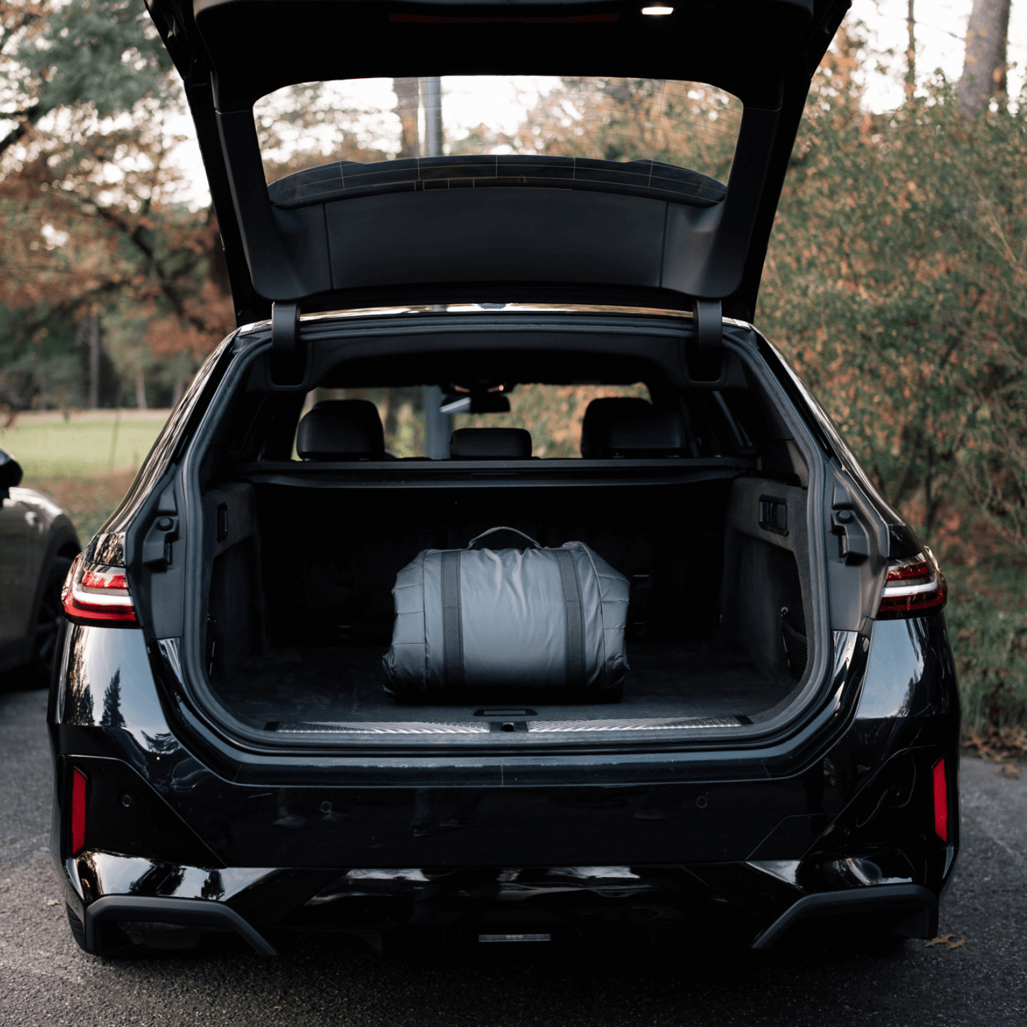 Black car with open trunk containing a Sportr Golf Travel bag, outdoors.