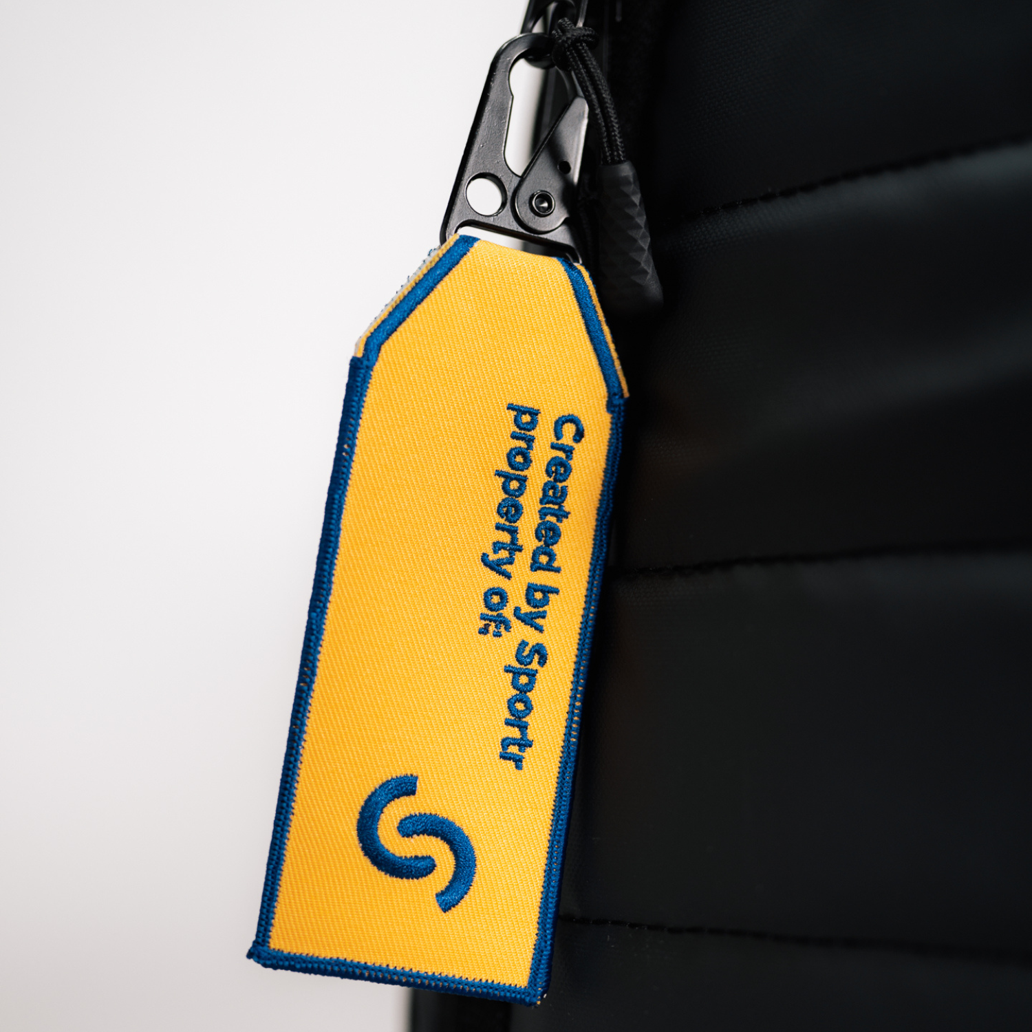 Yellow tag with blue text and logo attached to a black Sportr Golf Travel Bag
