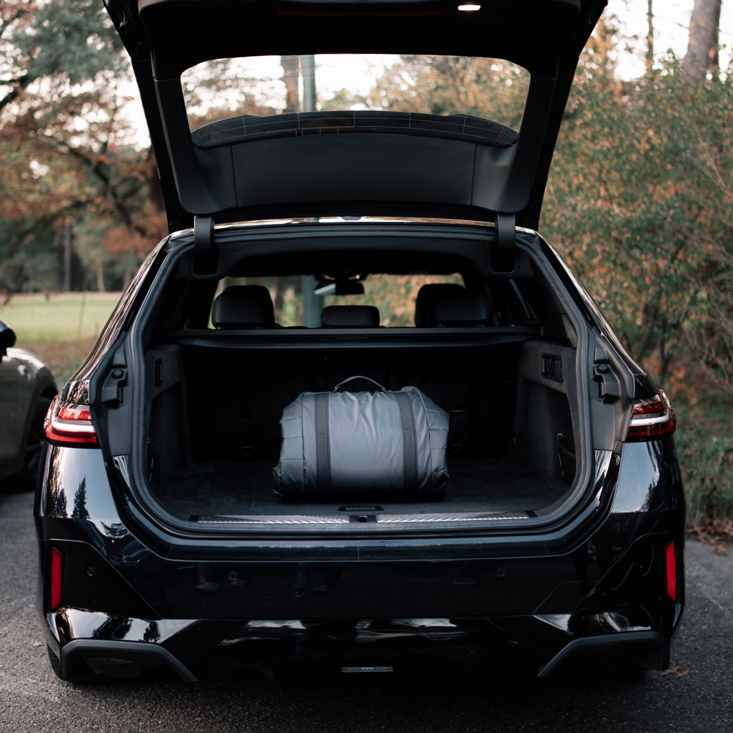 Black car with open trunk containing a Sportr Golf Travel bag, outdoors.